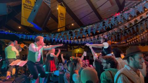 A photo of an Oktoberfest band playing in front of a large crowd, there is one lady dressed up in traditional German clothes.