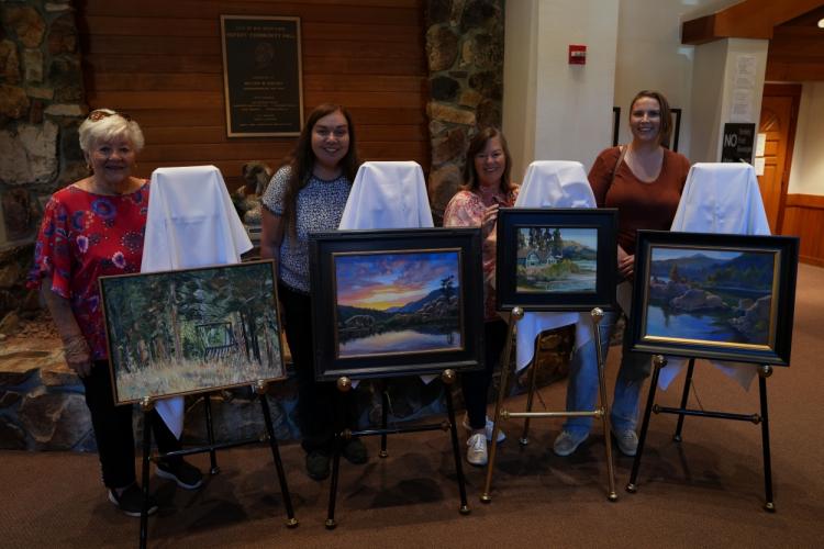The first through fourth place winners of the previous Plein Air competition, their paintings on display in front of them.