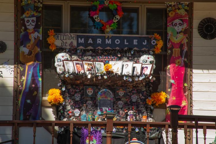 A 2025 Scarecrow & Dia de Los Muertos Display - the ofrenda has photos of people, candles, skeletons, and flowers.