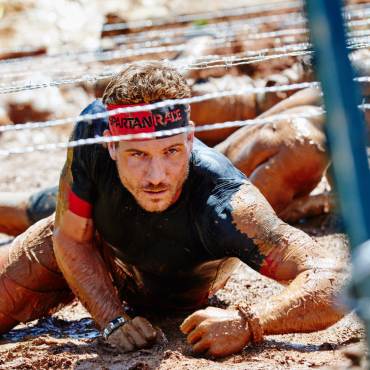 A Spartan racer crawls in the mud under barbed wire during the Spartan Trifecta Weekend in Big Bear Lake, CA.