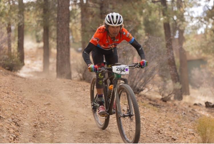 A photo taken of a mountain biker racing down a dirt path facing towards the viewer, her bike leaving a trail of dust behind.