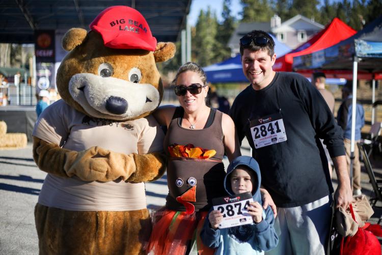 A mother, father, and child smile for a photo with the Big Bear Turkey Trot mascot during the Big Bear Turkey Trot.