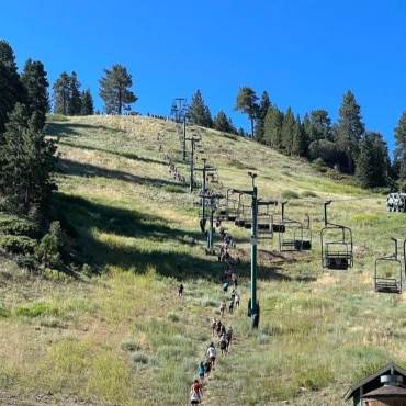 A distance photo of the Conquer The Wall competition participants hiking up the Snow Summit ski hill during summer.