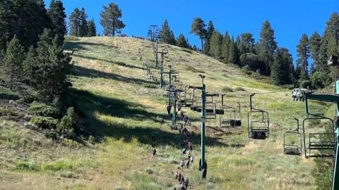 A distance photo of the Conquer The Wall competition participants hiking up the Snow Summit ski hill during summer.