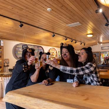 Four women are standing at a table having a toast of beer while in their Bear Costumes for the Big Bear Lake Bear Crawl.