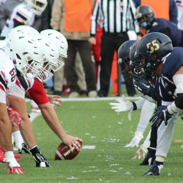 A photo of two football teams positioning in front of each other - one player is holding the football on the ground in front.
