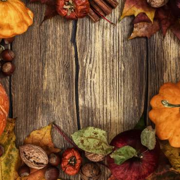 An aerial view of pumpkins, nuts, and leaves laid on a wooden slat table. The image represents Thanksgiving.