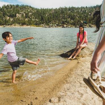 A boy splashes the water while playing on the shoreline of Big Bear Lake. His older sister and mother look on.