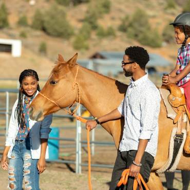 A mother and father lead a horse while their son enjoys a horseback ride.