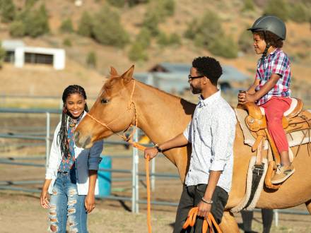 A mother and father lead a horse while their son enjoys a horseback ride.