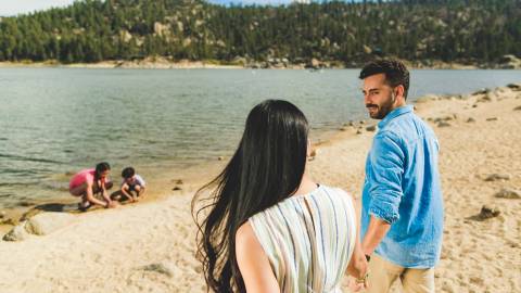 A mother and father walk hand in hand along the Big Bear shoreline towards their two children playing in the sand.