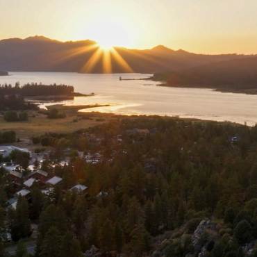 A photo of Big Bear Lake, the sunset gently shining across the lake, forest, and mountains.