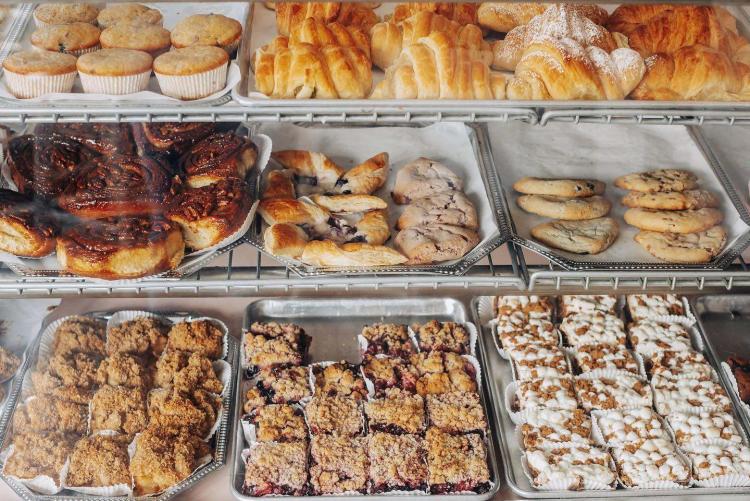 Three tiers of pastry sweets sit behind glass in a bakery in Big Bear Lake, CA. There are donuts, cinnamon rolls, and more.