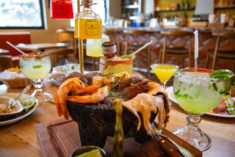 A Molcajete surrounded by other Mexican cuisine at Rosa's in Big Bear Lake - a tower of tequila bottles is seen in the back.