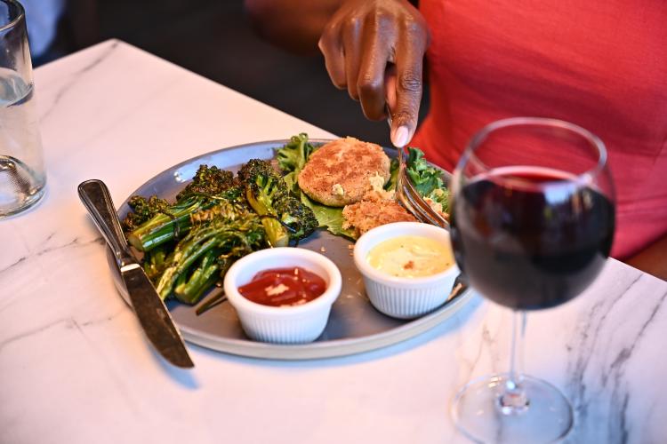 A diner cuts into her meal served at Stella Luna Restaurant in Big Bear Lake, CA. There is a glass of red wine served.