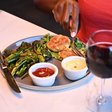 A woman's hand cuts food on a plate at a restaurant in Big Bear Lake. A glass of red wine sits by her plate.