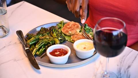 A woman's hand cuts food on a plate at a restaurant in Big Bear Lake. A glass of red wine sits by her plate.