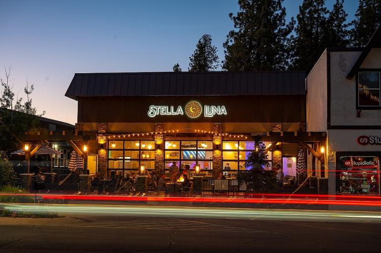 The exterior facade of Stella Luna Restaurant in Big Bear Lake, CA. It is nighttime, and a car is passing by.