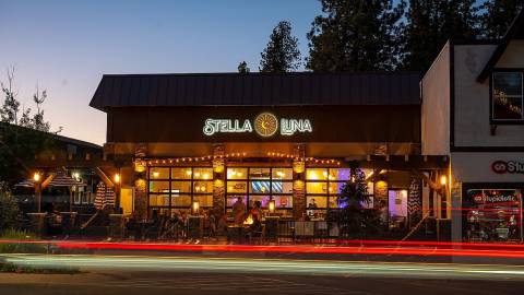 The exterior facade of Stella Luna Restaurant in Big Bear Lake, CA. It is nighttime, and a car is passing by.