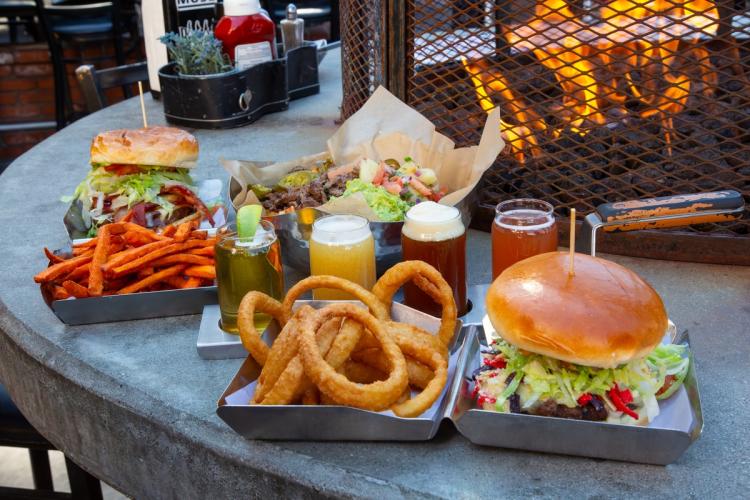 A photo of hamburgers and beers at Rock Burgers & Brews - there are sweet potato fries and onion rings in a clam shell box.