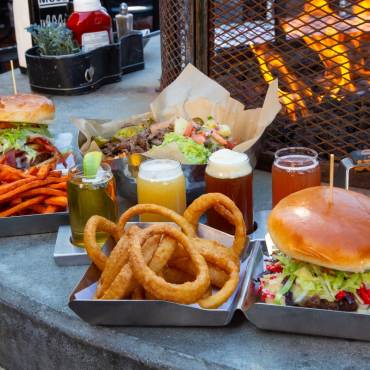 A photo of hamburgers and beers at Rock Burgers & Brews - there are sweet potato fries and onion rings in a clam shell box.