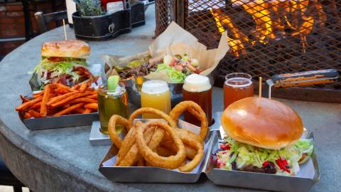A photo of hamburgers and beers at Rock Burgers & Brews - there are sweet potato fries and onion rings in a clam shell box.