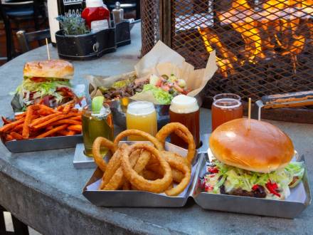 A photo of hamburgers and beers at Rock Burgers & Brews - there are sweet potato fries and onion rings in a clam shell box.