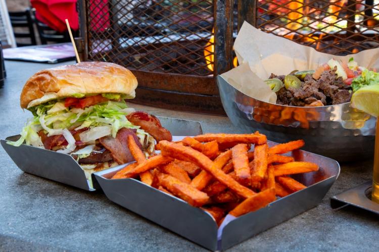 A photo of a hamburger with bacon at Fire Rock Burgers & Brews - there are sweet potato fries in a metal clam shell box.
