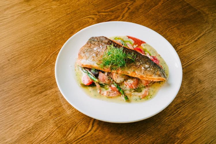 An overhead view of a cooked Rainbow Trout plated with sauce and vegetables - a wooden table is visible underneath the plate.