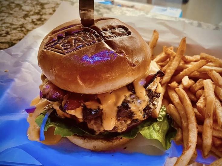 A photo of a hamburger and fries at Sandy's Sports Bar and Restaurant - the burger's bun is branded with Sandy's Logo.