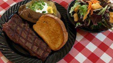 A photo of a side salad next to a black dish with a steak, Texas toast, and a baked potato from Wyatt's Grill and Saloon.
