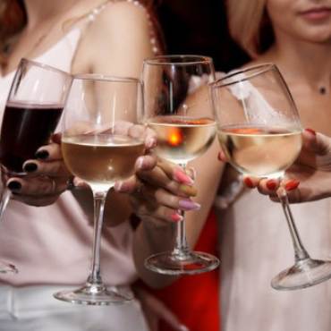 A photo of four women enjoying a toast with wine glasses - there is red wine seen in one of the glasses.
