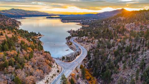 A drone shot of Big Bear Lake in fall, the sunset is peaking from behind the mountains and gently reflecting on the lake.