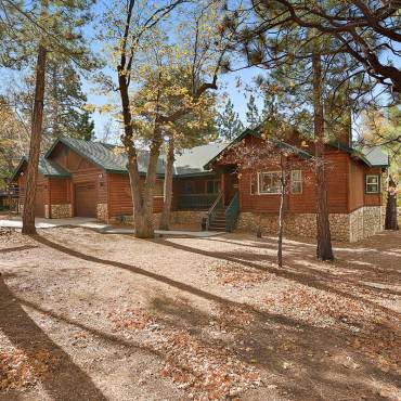 A log cabin styled vacation rental seen during fall - there are some trees with yellow leaves visible around it.