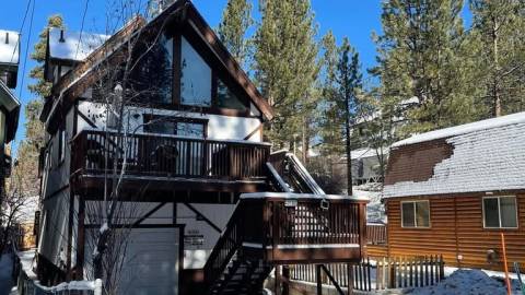 A snow covered cabin - it has a garage and stairs on the outside leading up to the second story with large glass windows.