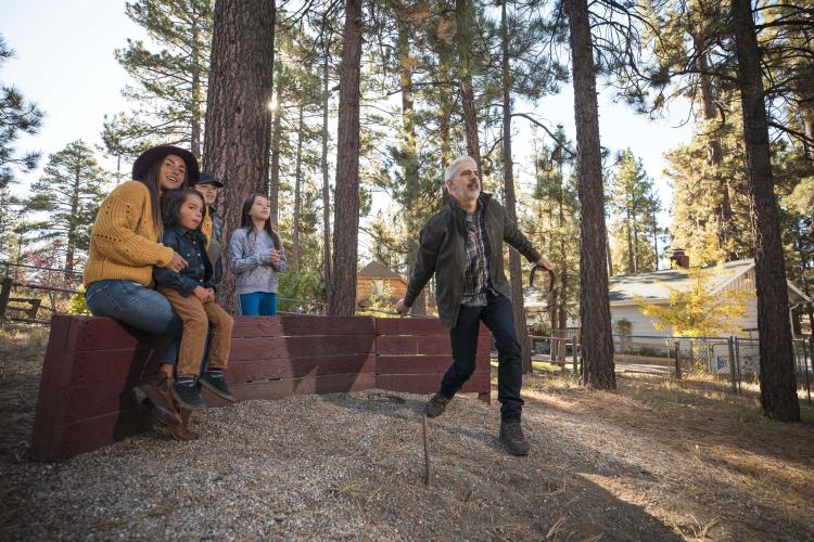A family watches on as Dad tosses a horseshoe in an outdoor pit in Big Bear Lake, CA. Big Bear lodging accommodations.