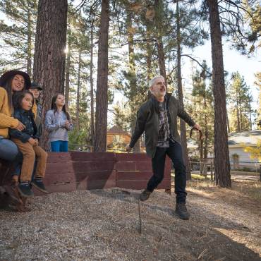 A family watches on as Dad tosses a horseshoe in an outdoor pit in Big Bear Lake, CA. Big Bear lodging accommodations.