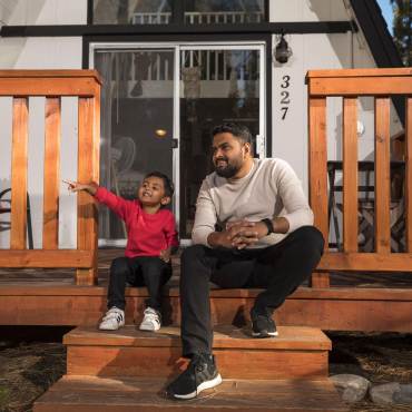 A Dad and Son sit on the steps of their Big Bear Lake rental home and admire their forest surroundings.