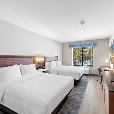 A hotel room interior, there are two large sized beds, a in counter sink and shelves, a television, and a desk workspace.