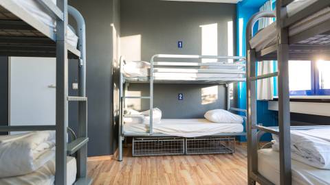 A photo of a hostel, there are bunk beds with storage crates underneath the lower cot.