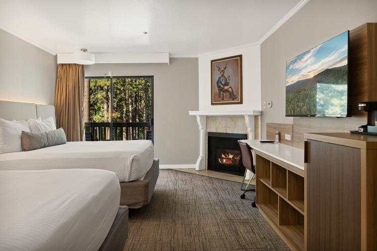 An interior photo of a Chateau Big Bear room, there is a television, two neatly done beds, a mini fridge, and a fireplace.