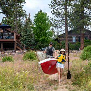 A couple carry paddleboards to Big Bear Lake from their lakefront home vacation rental.