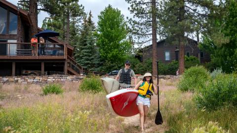 A couple carry paddleboards to Big Bear Lake from their lakefront home vacation rental.