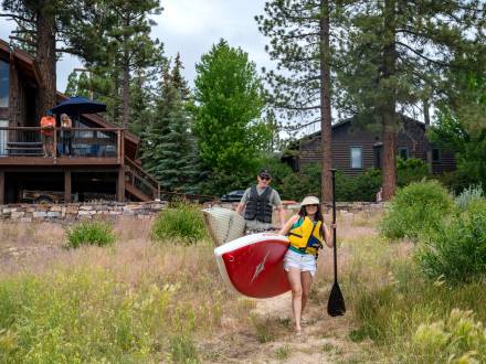 A couple carry paddleboards to Big Bear Lake from their lakefront home vacation rental.
