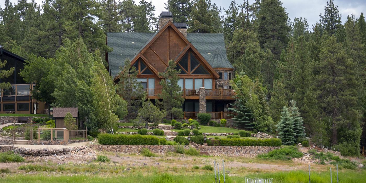 A beautiful brown house sits on the shore of Big Bear Lake. A kayaker paddles by in the water.