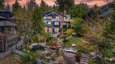 A navy blue three story house sitting on top a lush green hill - the sunset colored sky and forest are visible behind it.