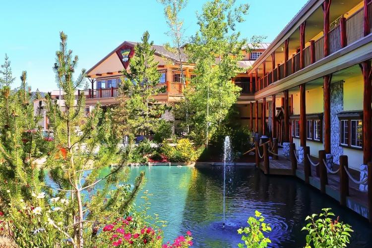 A side view of Holiday Inn Resort The Lodge at Big Bear Lake's entrance - there is a fountain in a pond with trees around it.