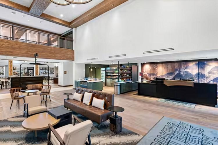 An interior shot of home2 suites - there is an open lounge with couches, chairs, and a bar with many drink shelves.