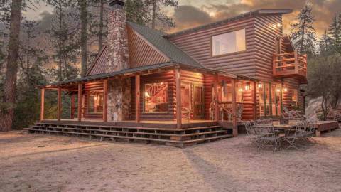 A Maltby Cabin in the forest sporting a rich wooden exterior with a stone chimney and crystal clear glass panes.