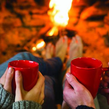 a couple holds cups of hot cocoa by the fire in Big Bear